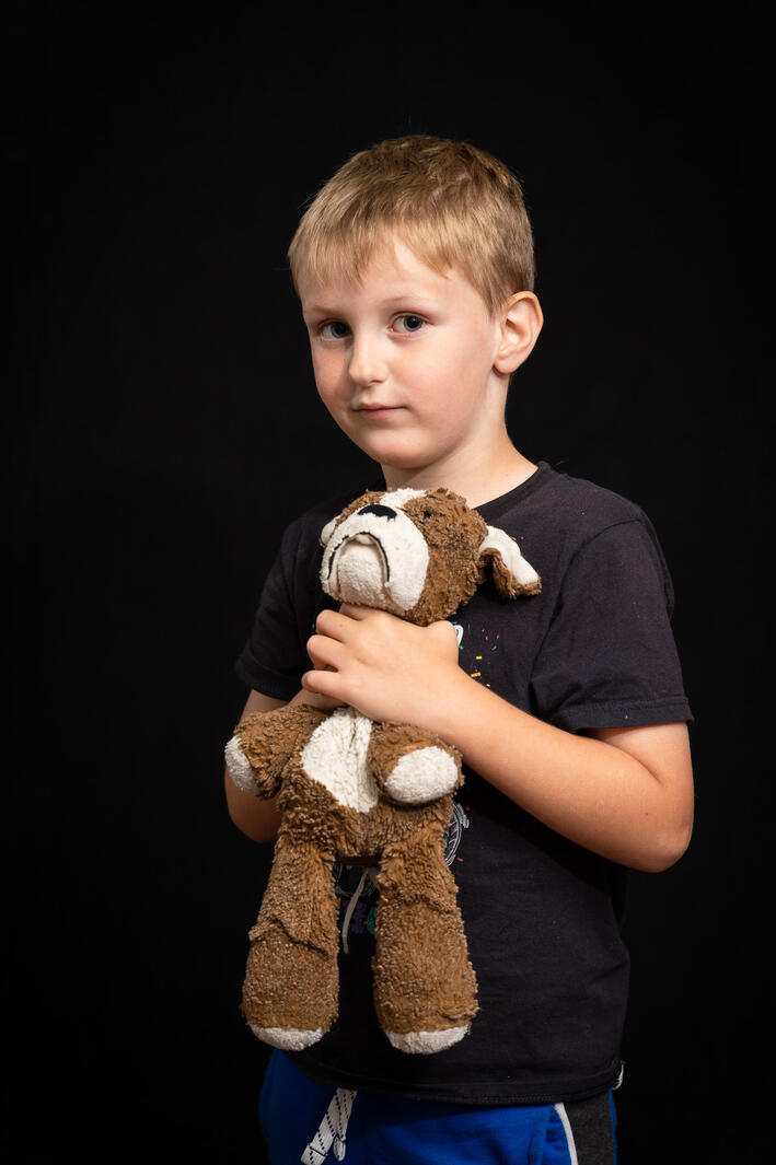 portrait of boy holding his stuffy dog on black background